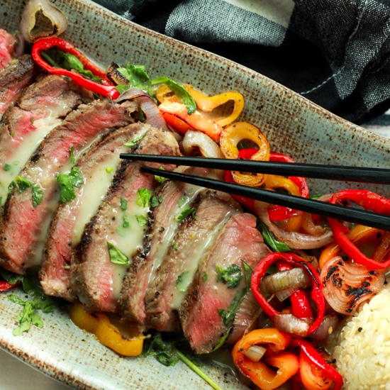Slices of grilled beef topped with roasted peppers, rice, and chopsticks on the side