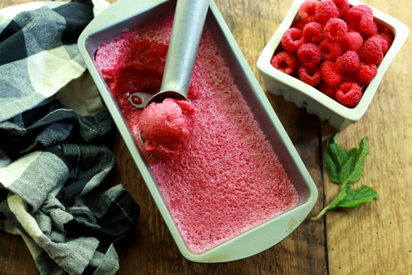 raspberry sorbet in a metal pan on a wooden board with a bowl of fresh strawberries along side