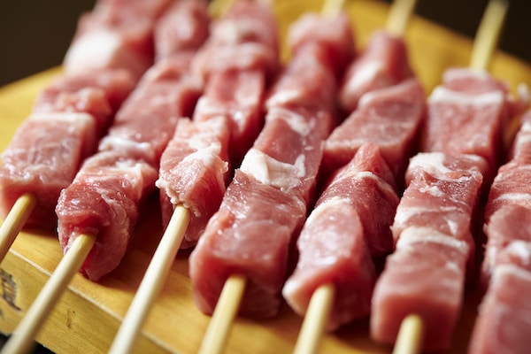Raw pork pieces on wooden skewers on a wooden board
