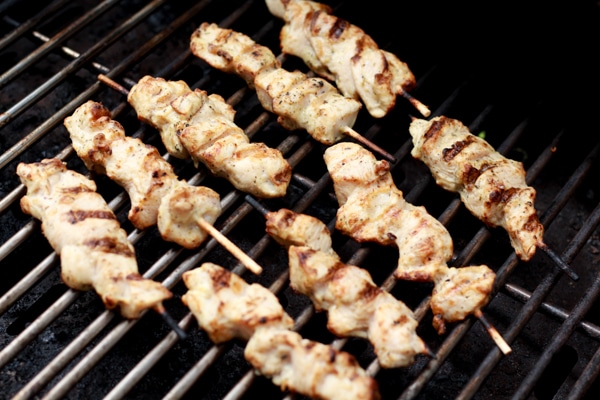 Tender chicken pieces threaded onto wooden skewers grilling on a hot grill.