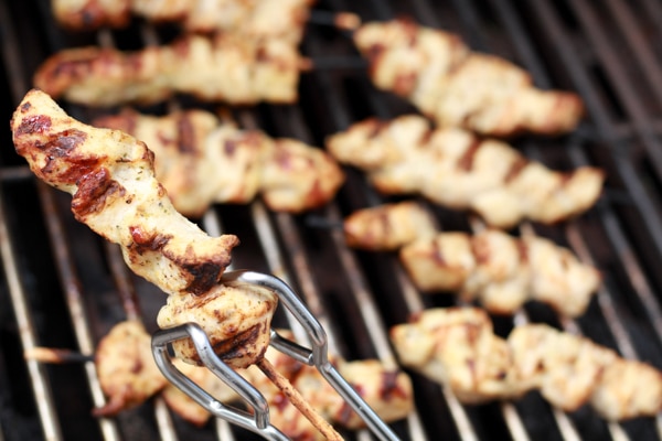 Tender chicken pieces threaded onto wooden skewers grilling on a hot grill.