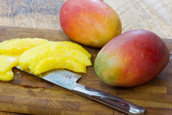 fresh mangos on a wooden cutting board with a knife and slices of mango