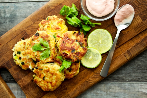 Mini crab cakes stacked on a wooden board with a side of aioli dipping sauce and fresh limes