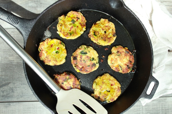 Fried mini crab cakes in a cast iron pan with a spatula on the side