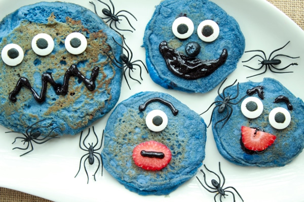 decorated blue monster pancakes on a white plate with black plastic spiders crawling on the plate