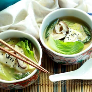 two bowls filled with wonton soup and chopsticks and a white spoon on the side