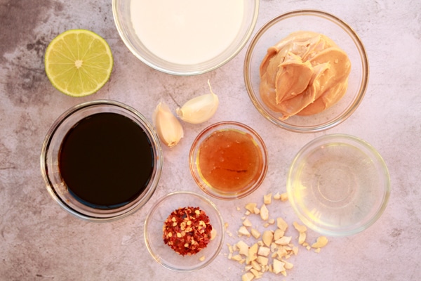 various ingredients for making peanut sauce on top of a gray surface