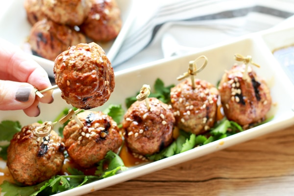 A lady's hand picking up a shrimp and turkey meatball on top of a narrow white plate with a side of Asian dipping sauce