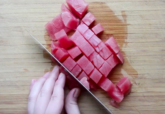 A woman chopping Ahi tuna into cubes on a wooden cutting board