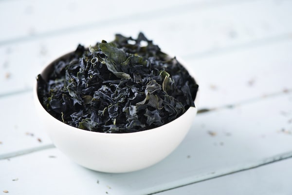a white bowl filled with dried seaweed on top of a white wooded board.