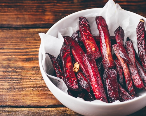 Oven baked beet fries in a white bowl on top of a wooden board