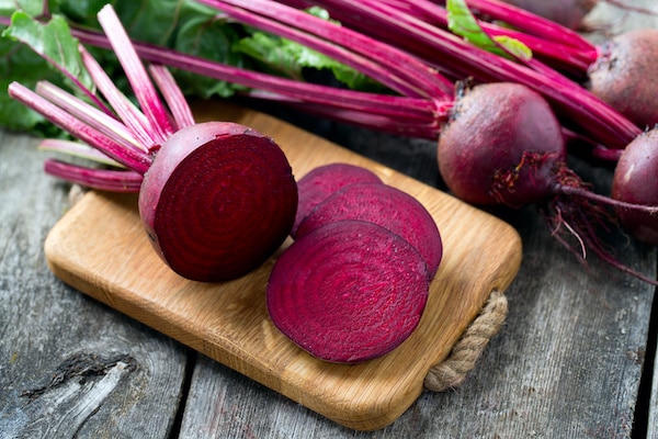 Fresh sliced red beetroot on wooden cutting board with whole red beets behind it.