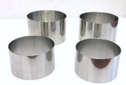 A set of four food stainless steel ring molds on a white board