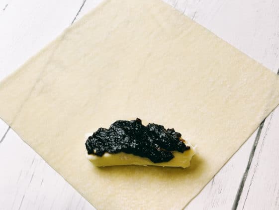 A wonton wrapper on a white board with a piece of brie and fig jam on top ready to be assembled.