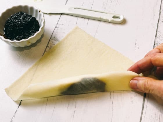 A woman rolling a wonton wrapper on a white board with fig jam on the side.
