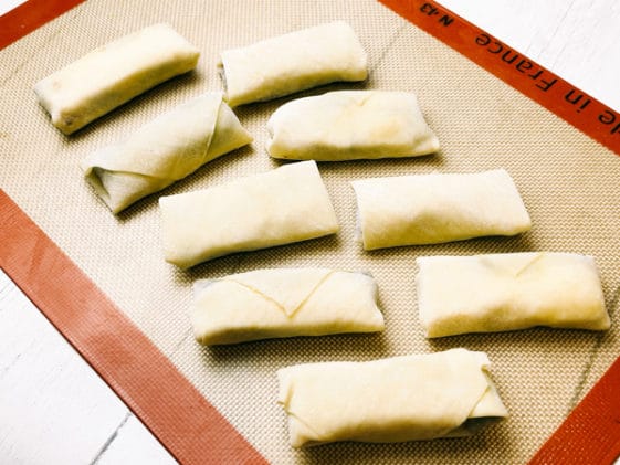 Two rows of uncooked spring rolls on a silicone mat.