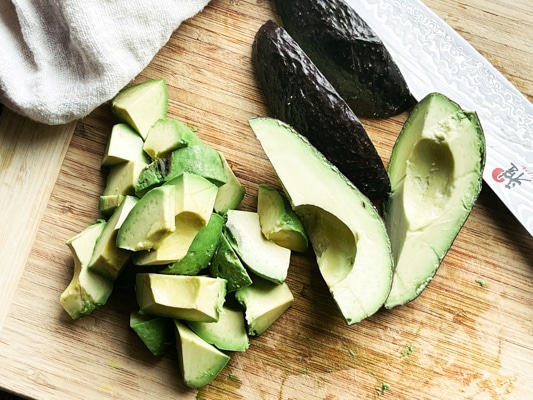Chopped avocado on a wooden cutting board with a chef's knife and napkin along side.