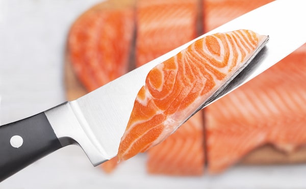 Raw fresh salmon fillet cut into slices and a piece on a chef's knife.