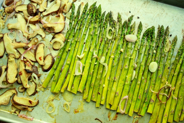 Roasted asparagus and shiitake mushrooms on a baking tray topped with shallot rings.