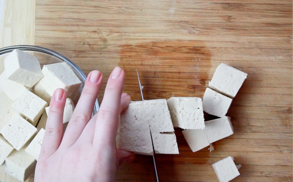 A woman cubing raw tofu on a wooden board.