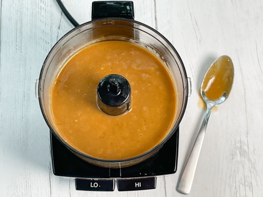 Miso ginger dressing inside a food processor with a spoon on the side, on top of a white board.