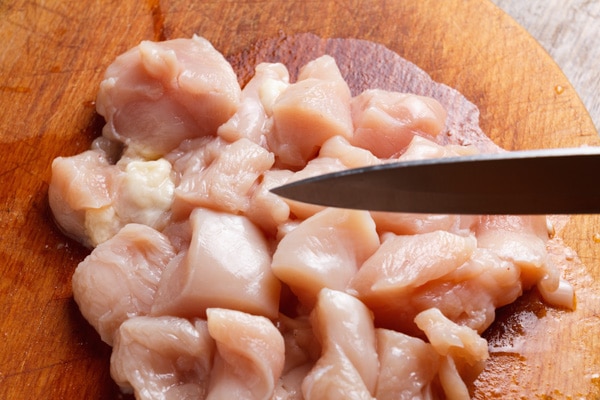 Fresh chicken cubes on a wooden cutting board with a kitchen knife.
