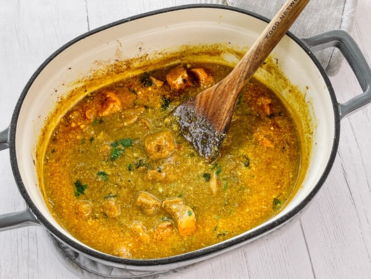 Thai Curry Chicken in a large gray pot with a wooden spatula inserted, on top of a white surface.