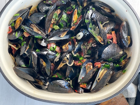 A large pot of steamed mussels tossed with pieces of smoky bacon, sliced shallots, slices of garlic, and fresh green herbs.