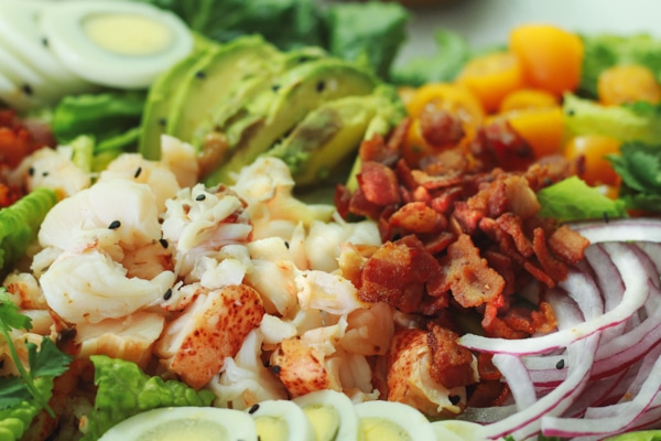 A close-up shot of vibrant lobster cobb salad on top of romaine greens.