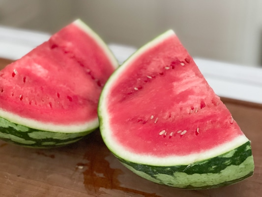 A watermelon split in half on top of a wooden board.