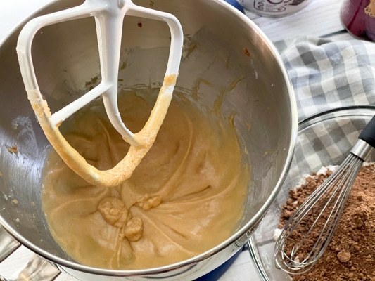 Batter for miso cupcakes in a silver mixing bowl with a white paddle and a bowl of cocoa powder on the side with a whisk.
