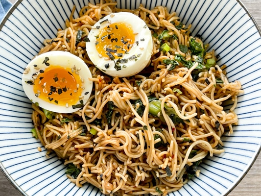 A striped bowl filled with ramen noodles topped with a runny egg.