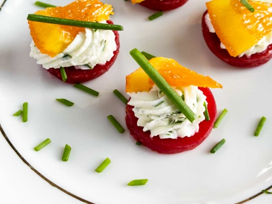A white plate with vibrant beet and goat cheese appetizer bites with sliced green onions on top.