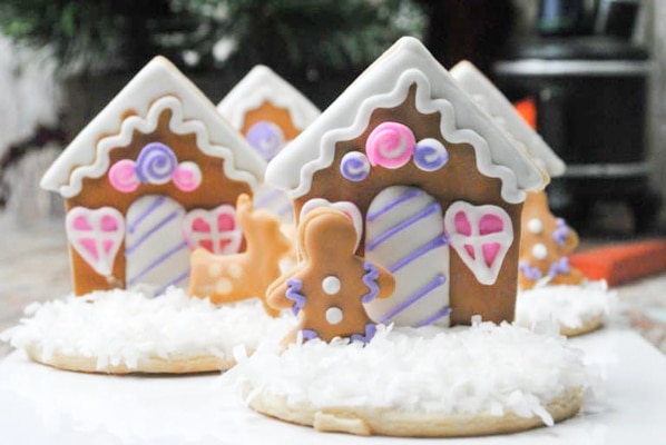 Adorable homemade decorated gingerbread house cookies with coconut flakes snow on top of a white surface.