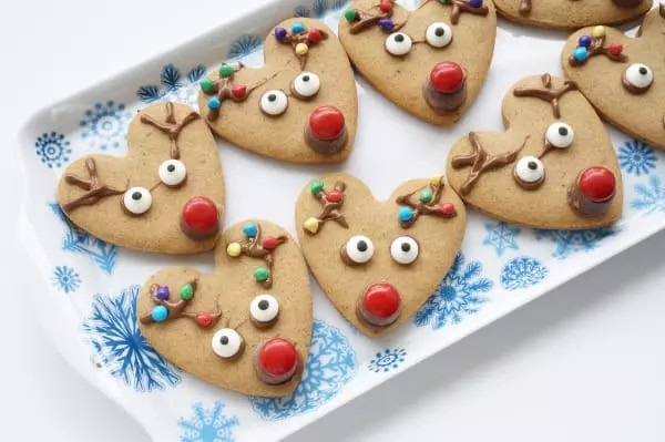 Heart-shaped cookies decorated to look like Rudolph the reindeer on top of a white plate with blue snowflakes.