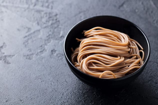 A black bowl filled with cooked soba noodles on top of a black surface
