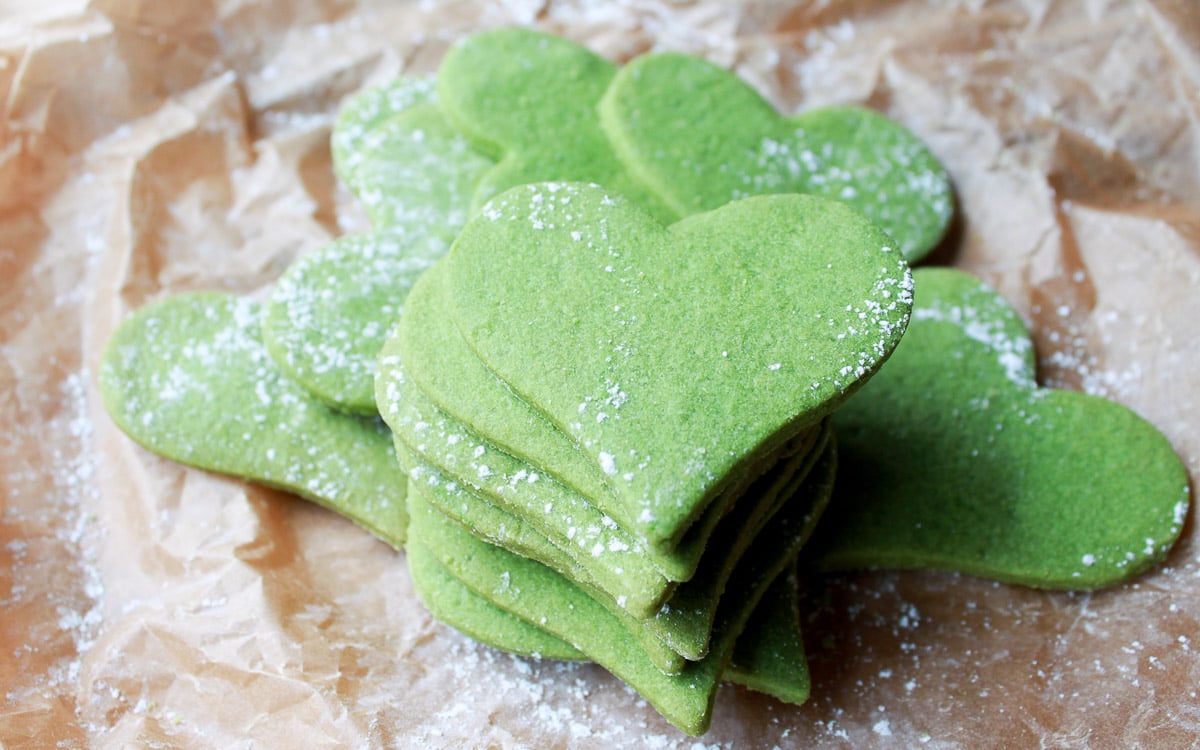 Vibrant green heart-shaped matcha cookies piled on top of each other placed on brown parchment paper.