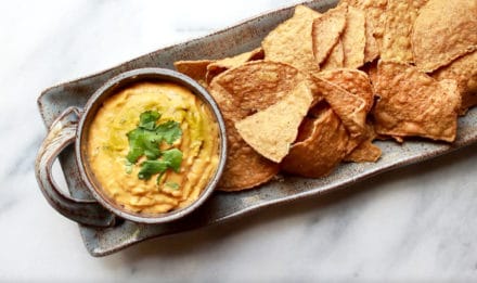 roasted thai butternut squash dip in a gray bowl on top of a gray serving platter with tortilla chips on the side on top of a marble surface