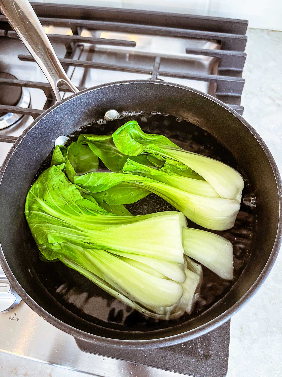 Baby bok choy boiling in water in a pot on the stove.