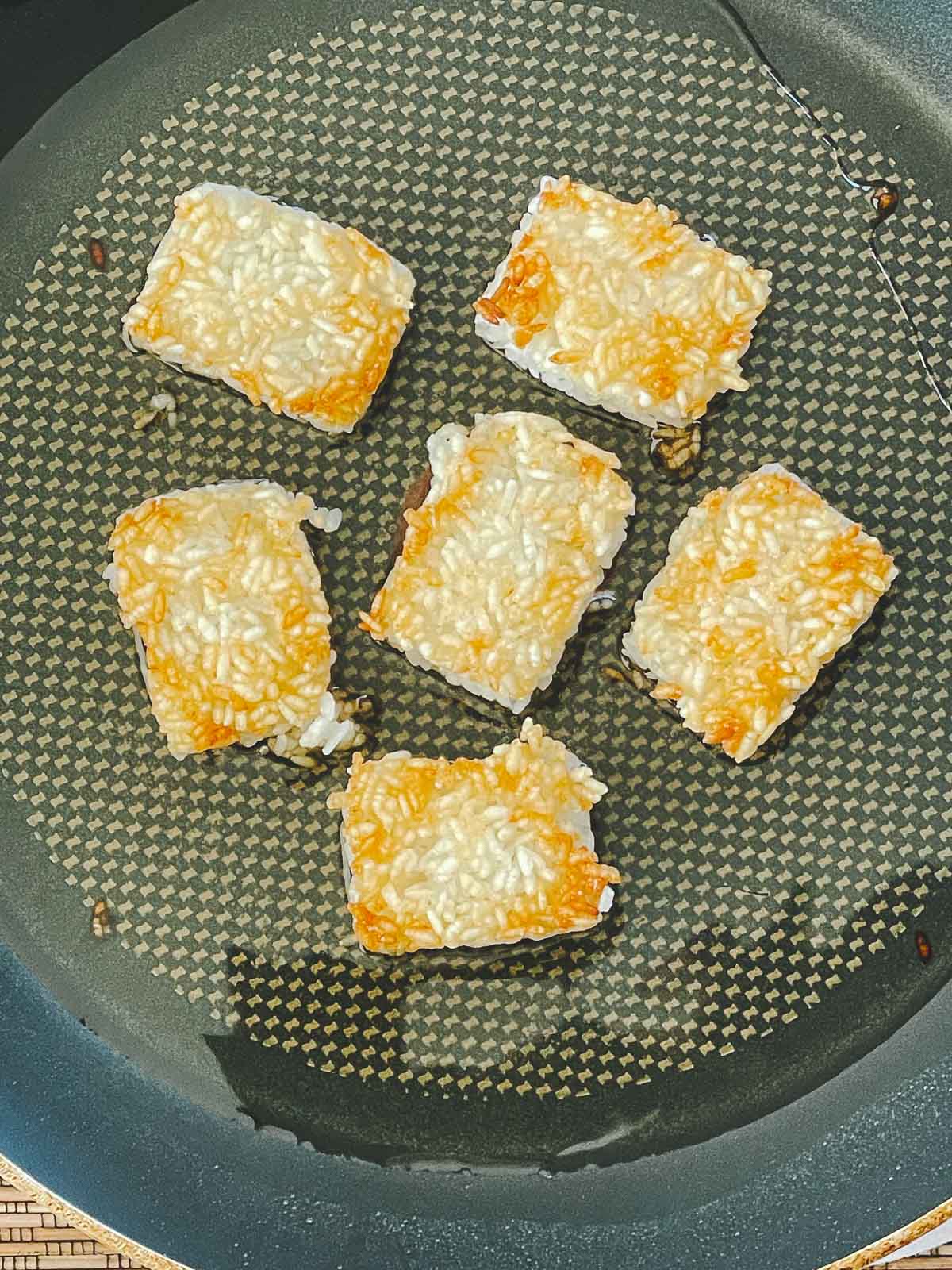 Golden crispy rice squares frying in a frying pan with oil.