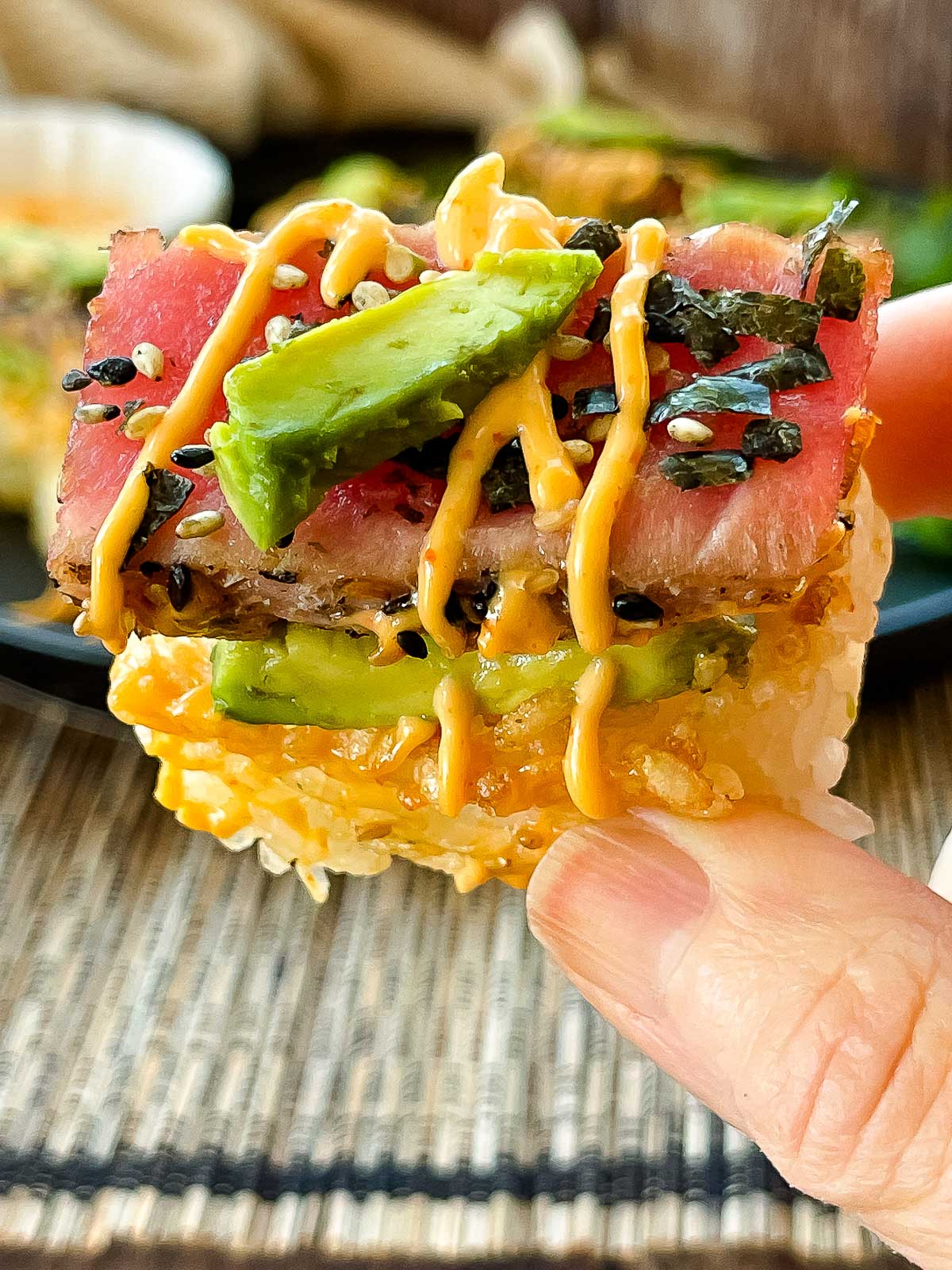 A hand holding up a piece of spicy tuna crispy rice drizzled with aioli sauce.