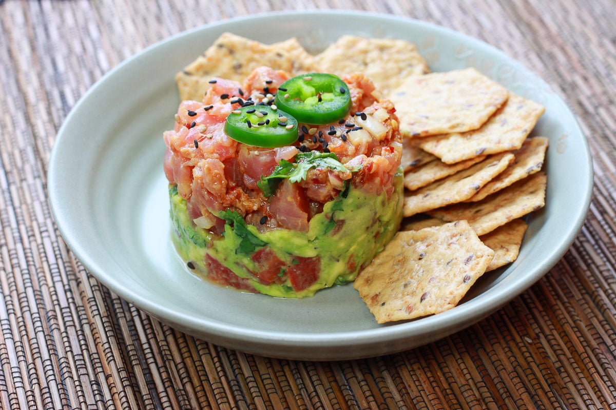 Vibrant Ahi tuna napoleon topped with jalapeño slices on a plate with sesame chips on the side.