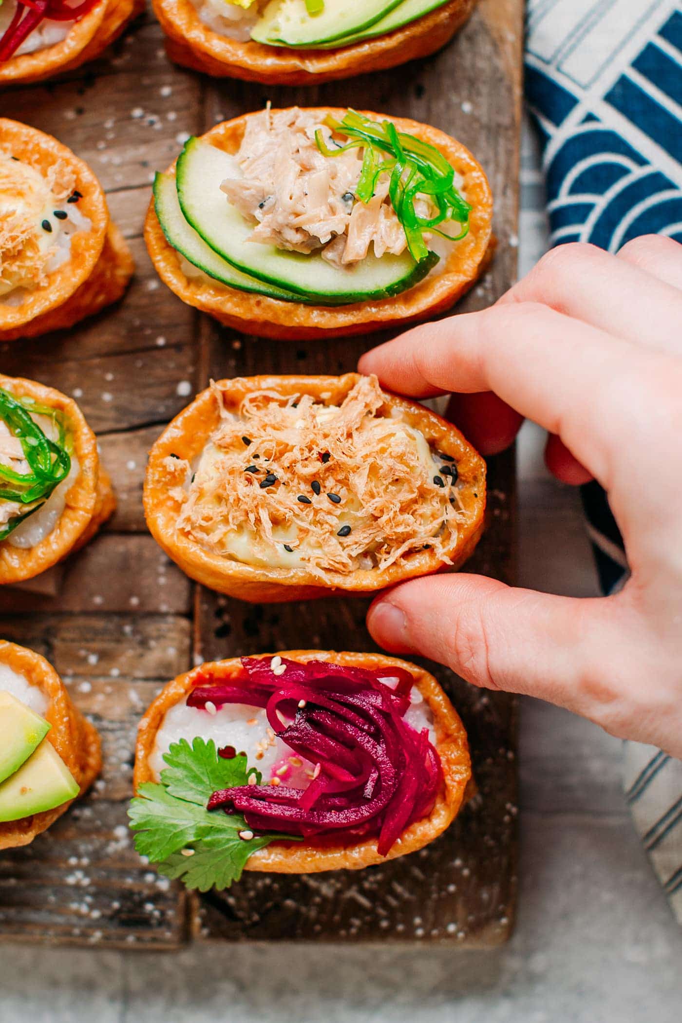 An assortment of sliced vegan inari sushi on a wooden board and a hand picking up a piece.