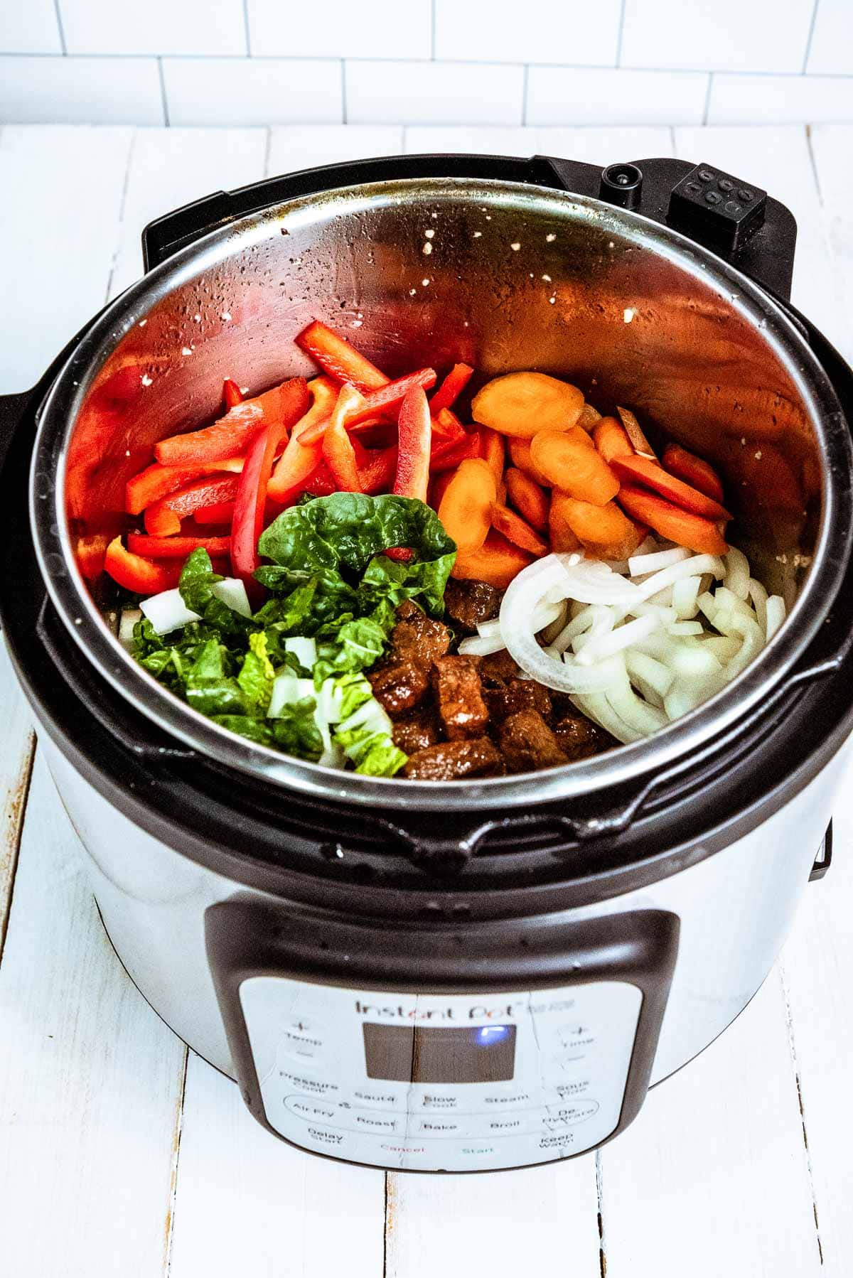 Vegetables and chunks of pork inside an Instant Pot ready to be cooked on top of a white board.