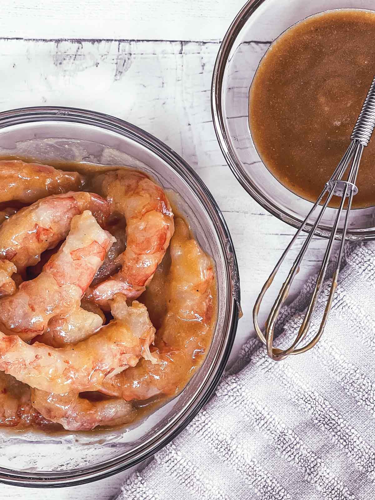 Shrimp marinating in miso sauce in a clear bowl and a smaller clear bowl with miso marinate and a whisk on top.
