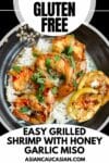 A black plate of grilled shrimp on top of white rice with charred lemon slices on top.
