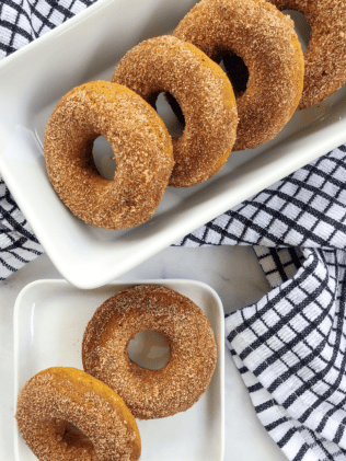 Baked pumpkin donuts on a white tray with a black and white napkin on the side.