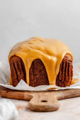 A loaf of pumpkin gingerbread  topped with a caramel glaze on top of a wooden cutting board.