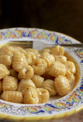 Homemade pumpkin gnocchi tossed in a butter sage sauce placed in a decorative Italian bowl with a fork.