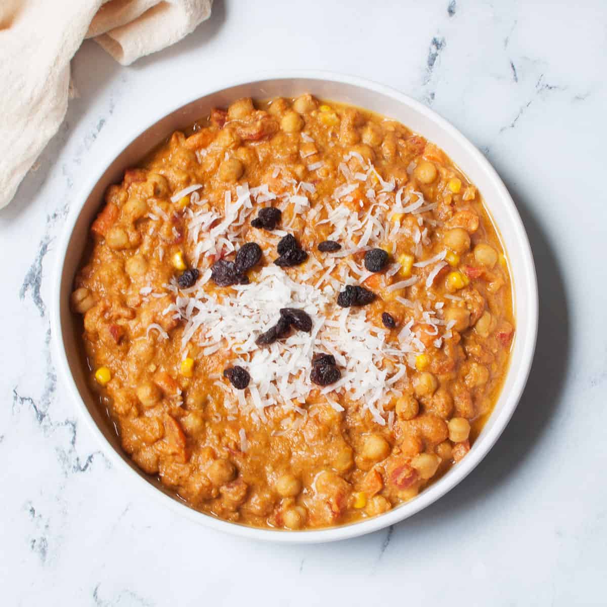 Pumpkin chickpea curry in a large white bowl topped with raisins and shredded coconut flakes.